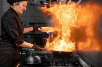 Woman Chef Cooking wok in the Kitchen. Cooking flaming wok with vegetables in the commercial kitchen. High quality photography.. Woman Chef Cooking wok in the Kitchen. Cooking flaming wok with vegetables in the commercial kitchen. 