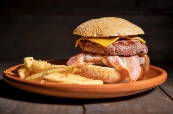 Premium grilled beef hamburger with bacon, cheese and French fries. Delicious American burger on wooden background. High quality photography. Premium grilled beef hamburger with bacon, cheese and French fries. Delicious American burger on wooden background. 