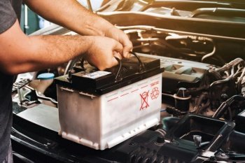 A auto mechanic carries a replacement car battery for car electrical maintenance