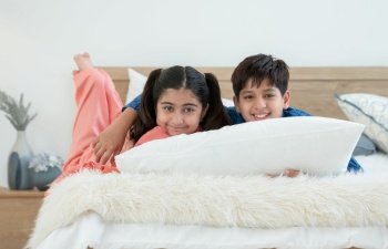 Two happy Indian brother and sister in traditional clothing lying on bed smiling and embracing each other at home, looking at camera. Siblings relationship concept