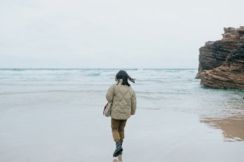 A young woman walking by the shore of the beach during a cloudy day, with copy space and liberty concept