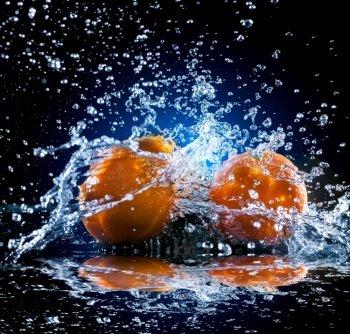 ripe oranges lying on the mirror in a spray of water on dark background. ripe oranges on mirror