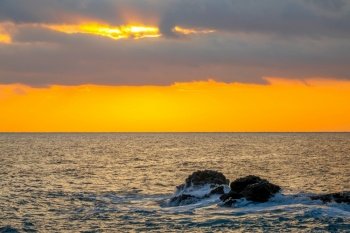 Amazing sunset colors in cloudy skies. Coastal stones in the calm sea. Amazing Sea Sunset Colours and Coastal Rocks