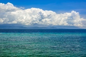 Indonesia. Sunny day. Turquoise water of a calm ocean. Surprisingly beautiful clouds over a distant island. Turquoise Sea Water and Amazing Clouds over the Island