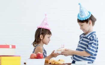 A caucasian boy giving a cake with candle to his little sister for celebrating her birthday