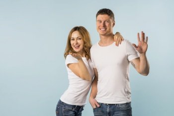 portrait smiling young couple waving hands against blue background