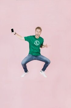 excited man with smartphone jumping pink backdrop