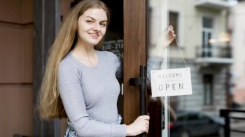 smiley woman putting up open sign coffee shop door