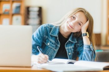 smiling teen making notes near laptop