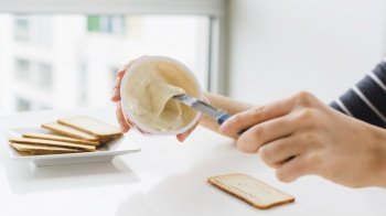 close up woman applying cheese spread bread with knife white table
