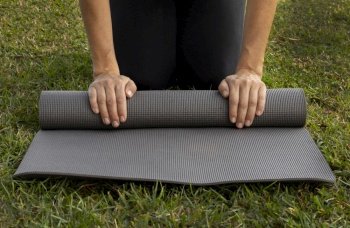 front view woman rolling yoga mat grass