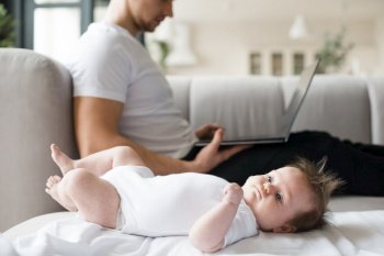 baby lying blanket near father using laptop