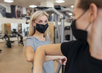 women with medical masks practicing elbow salute gym