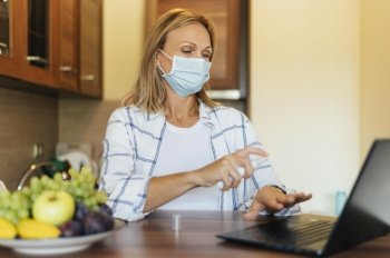 woman home during quarantine with medical mask laptop