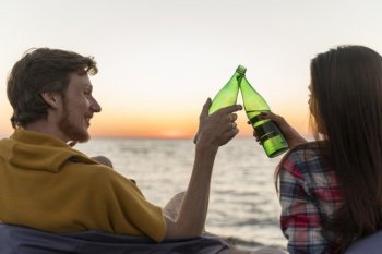 man woman toasting with beer bottles sunset