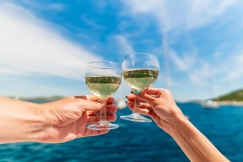 Couple holding two glasses of white wine over ocean background with yacht on background - shallow depth of field. Couple holding two glasses of white wine over ocean background with yacht on background