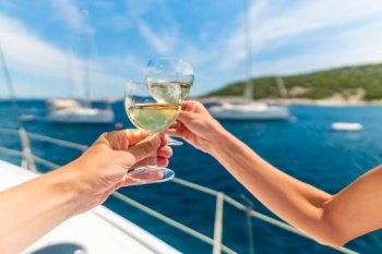 Couple holding two glasses of white wine over ocean background with yacht on background - shallow depth of field. Couple holding two glasses of white wine over ocean background with yacht on background
