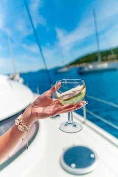 Woman holding glass of white wine over ocean background with yacht on background - shallow depth of field. Woman holding glass of white wine over ocean background with yacht on background