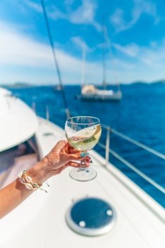 Woman holding glass of white wine over ocean background with yacht on background - shallow depth of field. Woman holding glass of white wine over ocean background with yacht on background