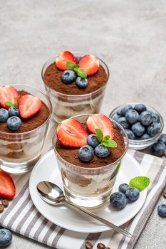 Classic tiramisu dessert with blueberries and strawberries in a glass on concrete background or table. Classic tiramisu dessert with blueberries and strawberries in a glass on concrete background