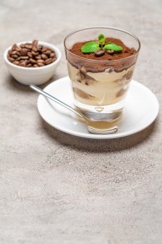 Classic tiramisu dessert in a glass cup on plate and coffee beans on concrete background or table. Classic tiramisu dessert in a glass cup on plate and coffee beans on concrete background