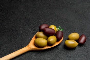 wooden spoon full of olives on dark concrete background. wooden spoon with olives on dark concrete background