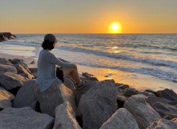 Woman sitting on rocks while watching a golden sunset. Location is Gulf of Mexico in Florida state 