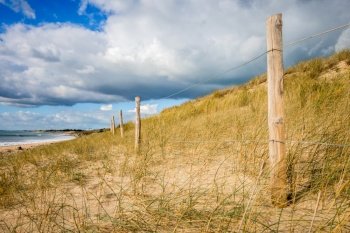 Sand dune and fence on a beach, Re Island, France. Cloudy background. Sand dune and fence on a beach, Re Island, France