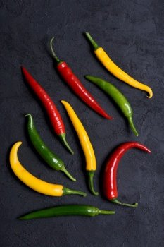 Assoted different colored chilli peppers on dark background