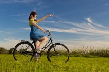 Happy girl with a old bicycle and pointing to something, in a green meadow