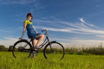 Happy girl with a bicycle in a green meadow