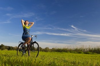 Happy girl over a bicycle and looking the view, in a green meadow