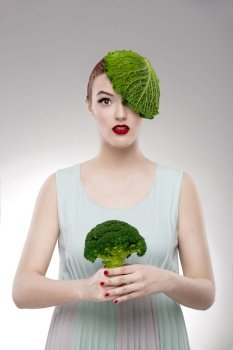 Portrait of a woman illustrating a vegan concept with a cabbage on the head and holding a broccoli. Vegan Girl