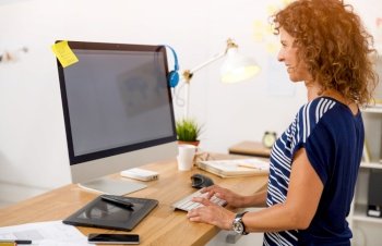 Middle age designer working on a desktop at her office