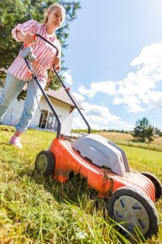 Gardening, taking care of house backyard, agricultural concept. Female person mowing green lawn with lawnmower in sunny day.. Woman mowing green grass