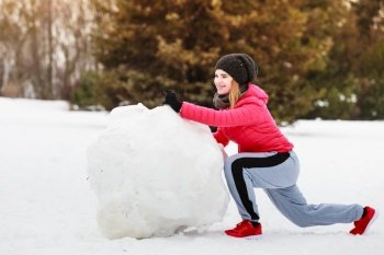 Woman wearing sportswear during winter weather with snow making big snowball for snowman. Woman wearing sportswear during winter