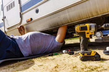 Man lying on ground, repairing bottom of the caravan vehicle.. Man repairing bottom of the rv caravan