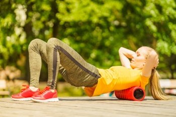 Young woman exercises in park, using gym accessory, foam roller for muscle massage. Staying fit and healthy.. Girl doing exercises outdoor, using roller