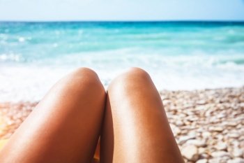 Closeup photo of a women’s legs lying down on stony seashore, body part, young female with pleasure taking sunbath, conceptual photo of summer vacation on the beach