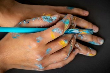 Closeup photo of a hands of talented artist with paintbrush stained with paint over gray background, moments of inspiration concept