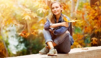 Nice female in bright sunny day sitting in the park and enjoying beautiful autumn nature and wonderful weather, with pleasure spending weekend outdoors