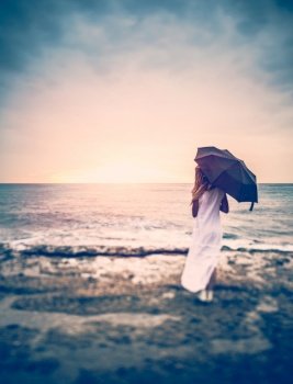 Sadness concept, rear view of a woman with umbrella on the beach, girl in overcast weather looking on the stormy sea, loneliness