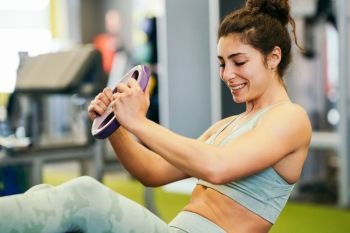 Sporty young female, wearing sportswear, on yoga mat doing situps with plate weights in gym. Fitness woman doing abs crunches.. Young sportswoman on yoga mat doing situps in gym.
