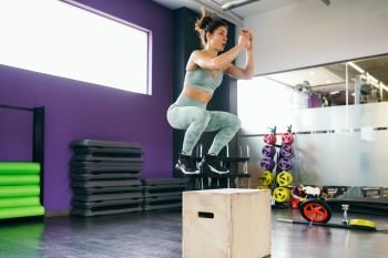 Fitness woman jumping onto a box as part of exercise routine. Caucasian female doing box jump workout at gym.. Caucasian female doing box jump workout at gym.