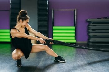 Young and athletic woman using training ropes in a gym. Fitness concept.. Young and athletic woman using training ropes in a gym.