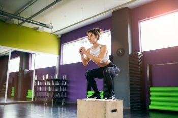 Athletic woman doing squats on box as part of exercise routine. Caucasian female doing box jump workout at gym.. Athletic woman doing squats on box at the gym