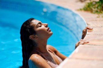 Beautiful Arab woman relaxing in swimming pool with eyes closed. Girl with healthy tanned skin and wet hair enjoying Summer Sun.. Beautiful Arab woman relaxing in swimming pool.