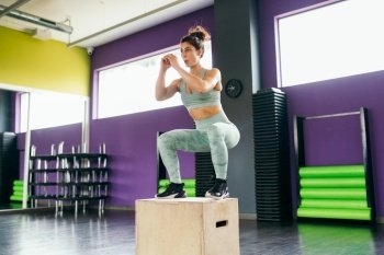 Fitness woman jumping onto a box as part of exercise routine. Caucasian female doing box jump workout at gym.. Fitness woman jumping onto a box as part of exercise routine.
