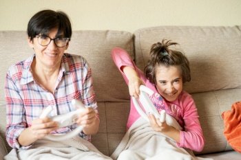 Mother and daughter playing video games at home with a wireless console. Mother and daughter playing video games at home