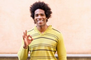 Black man with afro hair putting a funny expression outdoors. Ok gesture with his hand. Black man with afro hair putting a funny expression